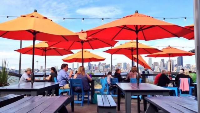 orange umbrellas offer a covered outdoor dining experience at Marination in Seattle, with the skyline in the background