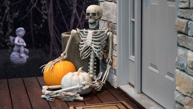 A skeleton and a pumpkin on a front stoop