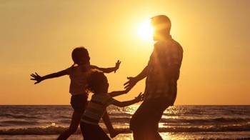 Kids run toward a father during a sunset with the ocean in the background