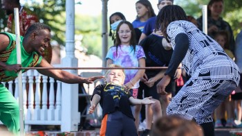 a boy goes under a limbo stick while people help and cheer him on at the Big E Boston festival in Fall
