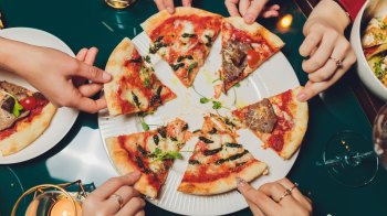 hands reaching to take slices of pizza from plate