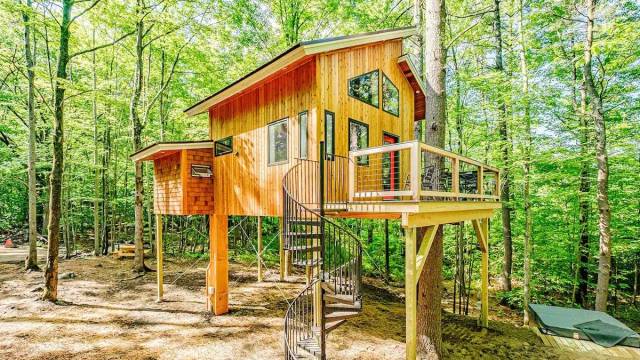 Treehouse rental with a spiral staircase and deck in a well lit treed area