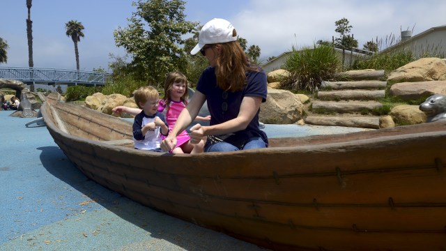 Mother and two children sitting in a boat in a park