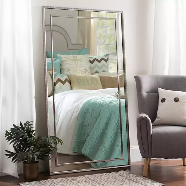 Silver full-length mirror standing against a wall