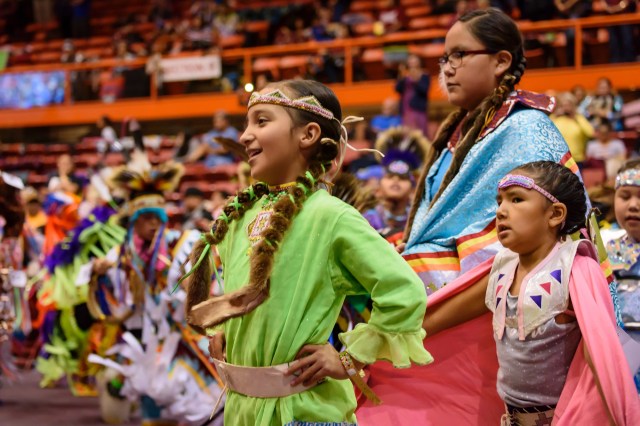 Native American children dressed in traditional clothing for a powwow.