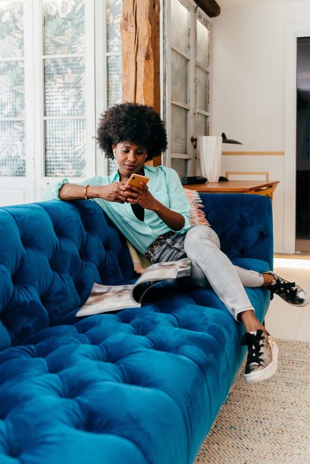 A woman sits on a blue couch looking at her cell phone