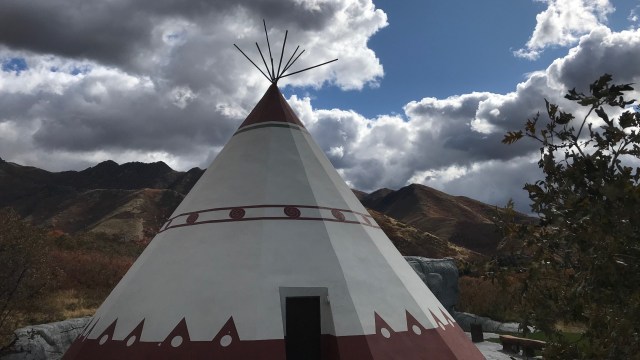 Large white and brown teepee under a blue sky with white clouds.