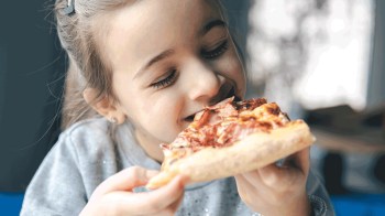 A kid takes a bite of a piece of pizza
