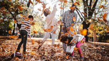 family enjoying throwing leaves, which is a fun fall bucket list idea