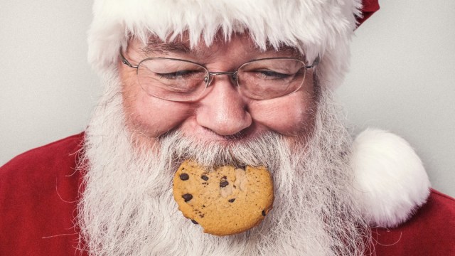 a Santa smiles with a cookie in his mouth