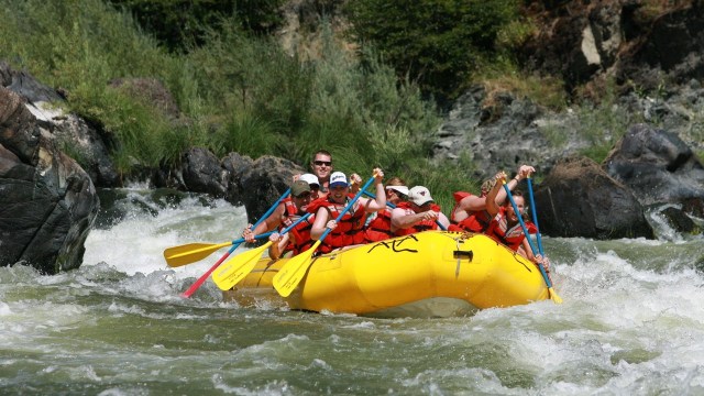 Group of rafter in red vests paddling on whitewater river in a bright yellow raft.