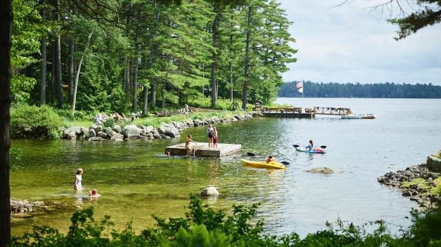 Lakeside scene with people in kayaks, swimming, having fun in the water.