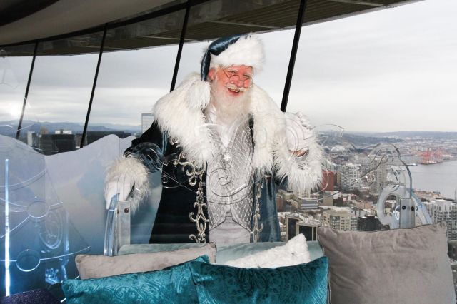 Santa photos seattle include this santa atop the Space Needle pictured next to his clear sleigh
