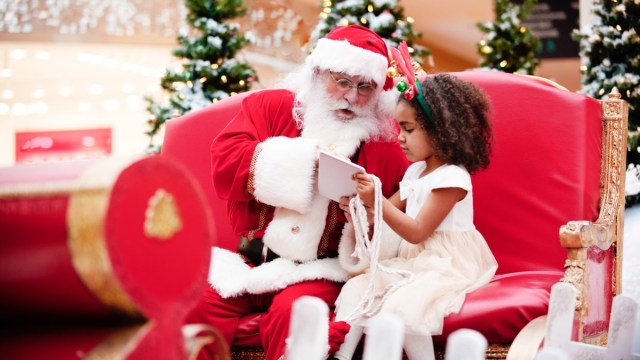 a young girl sits next to santa in his red sleigh during a Santa Atlanta experience at Christmas time