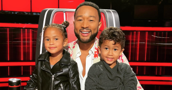 John Legend with both his kids on his lap in his red chair on set of The Voice