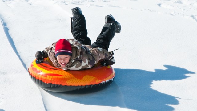 a smiling boy dressed for winter comes down a snow tubing hill