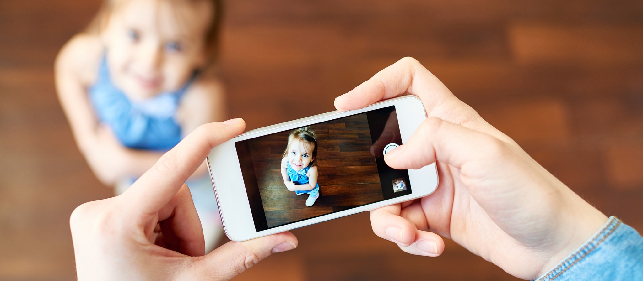 Little girl posing and mother photographing her with smart phone