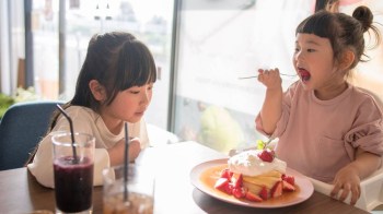 a girl eats a waffle covered with strawberries and whip cream while a friend looks on, a comfort food in dc favorite
