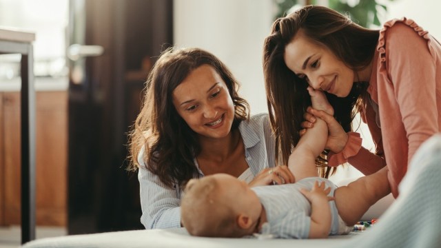 two moms play peek a boo, games for babies, with a newborn on a bed