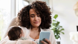 a mom scrolls on her phone checking out atlanta instagram influencers while holding a baby in a rocking chair
