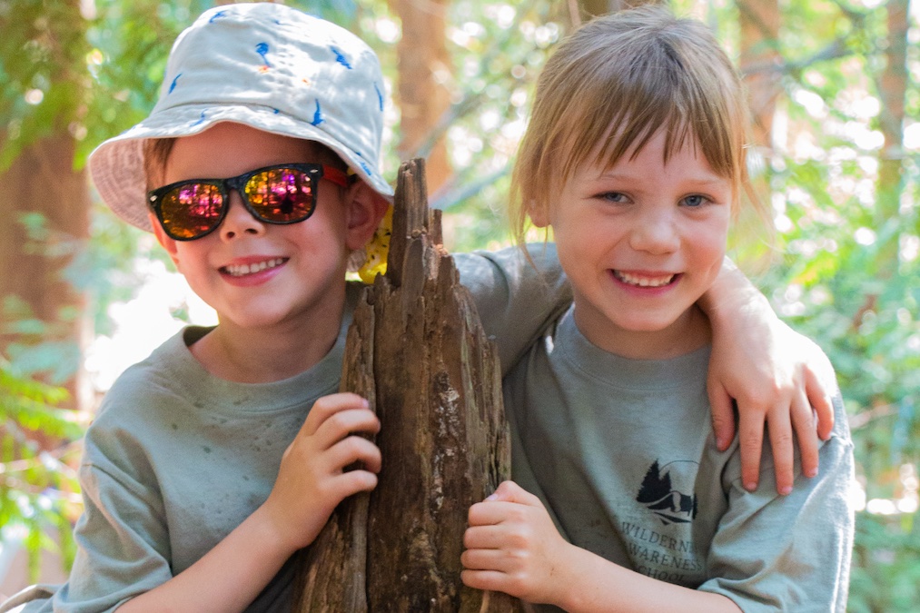 two kids in green shirts around a tree at a Seattle summer camps, wilderness awareness school