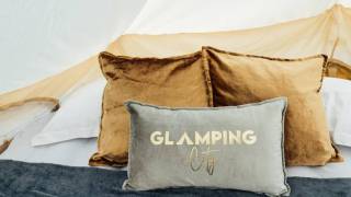 Pillows on bed inside glamping tent. Front pillow says Glamping City.