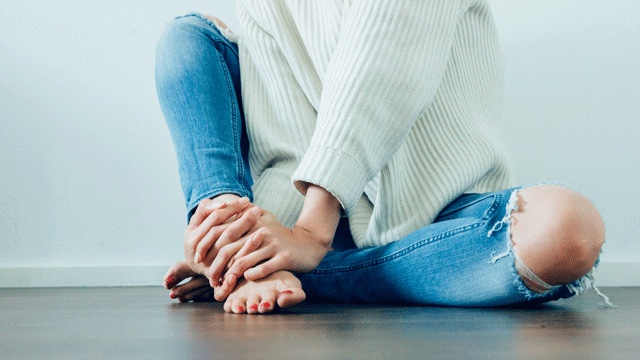 something bodies changes after pregnancy include feet getting bigger like this woman holding feet wearing jeans and a white sweater