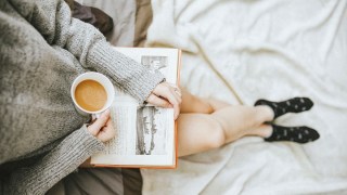 a woman is reading a book with a cup of coffee and socks on in a cozy location