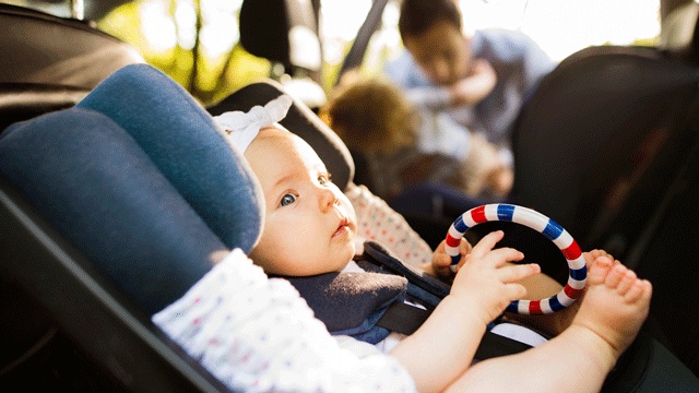 a baby sits in a car seat with a teether in her hand, ready for a road trip