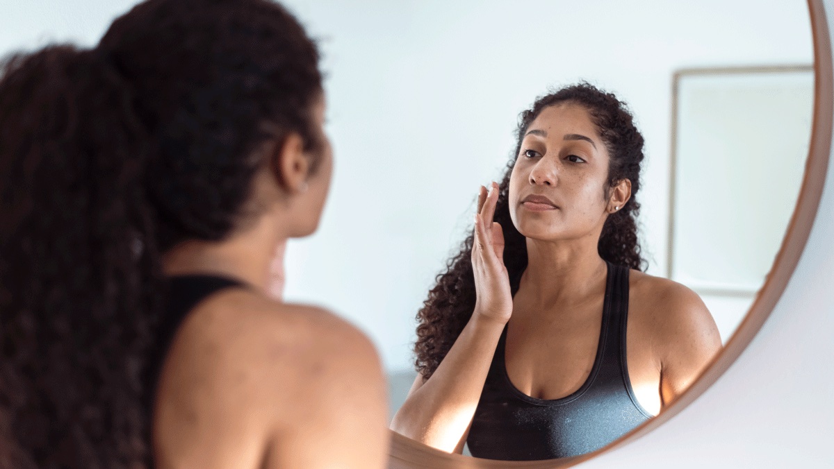 A woman looks in the mirror and applies cream to dark spots, one way the body changes after pregnancy