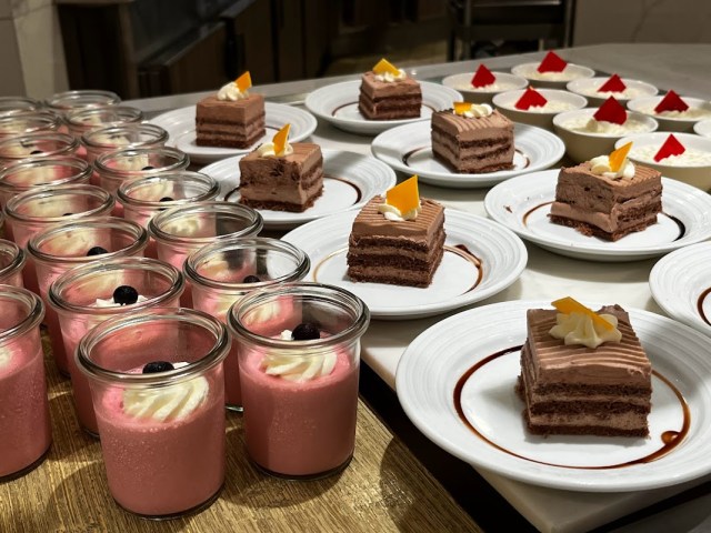 Jars of pink pudding with shipped cream and berry on top, chocolate cake on white plates and bowls of rice pudding laid out at the buffet on Sky Princess cruise