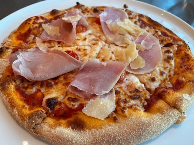 Individual pizza with prosciutto and cheese on white plate