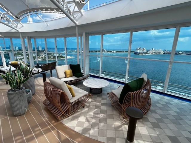 Padded seating surrounding a table. Floor to ceiling windows overlook bow area of the Sky Princess cruise ship.
