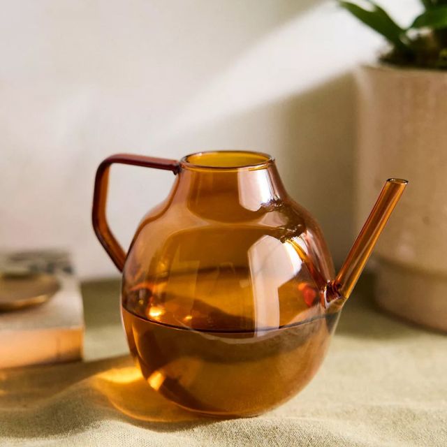 amber glass watering can half full of water on table top