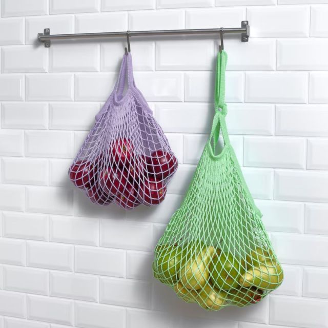 two mesh bags filled with fresh fruit hung on a metal hook in a kitchen