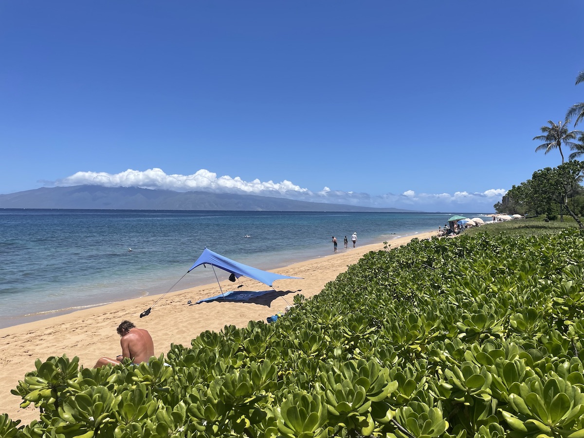 a beach with an island in the background and a blue sunshade westin Ka'anapali ocean resort