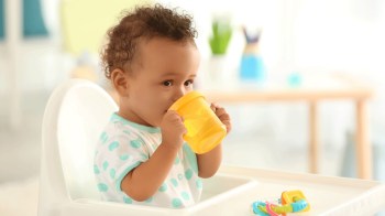 a little boy drinks from a sippy cup in a high chair, some would consider this baby gear to borrow