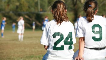 two girl soccer players sitting on a bench on the sidelines