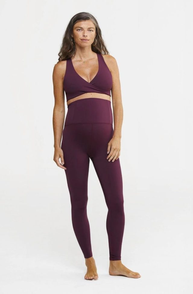 pregnant woman standing in burgundy leggings and sports bra