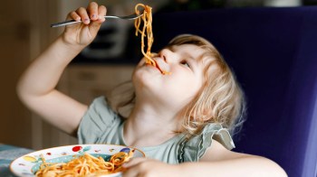 a girl eats spaghetti held above her head