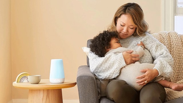 a mother snuggles a toddler on a couch, nearby baby sound machine in blue is on a neutral colored table