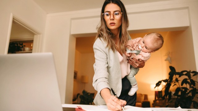 a busy mom holding a baby types on a computer returning to work after maternity leave
