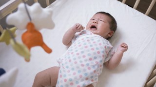 a baby in a onesie cries in her crib during a sleep regression