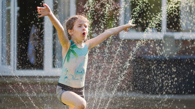 picture of a girl playing in the sprinkler, one of the best things to do in summer
