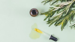 a dropper with oil dripping out beside a few sprigs of rosemary in regards to postpartum hair loss treatments