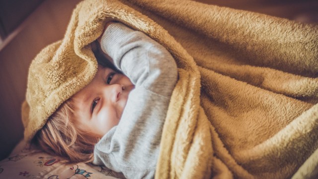 A kid wrapped in a blanket because wrapping your kid like a burrito is one of the best sensory moves to calm down kids before bed