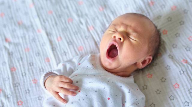 a baby yawning in her crib while falling asleep