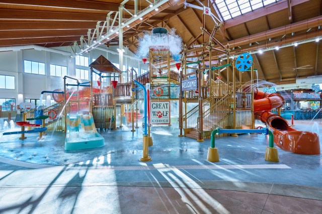 Children's lay area at indoor water park with colorful slides and games amid water fountains and pool area.
