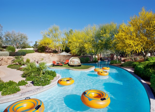 Yellow tubes floating in a lazy river pool feature with a private island filled with daybeds and umbrellas in the background.