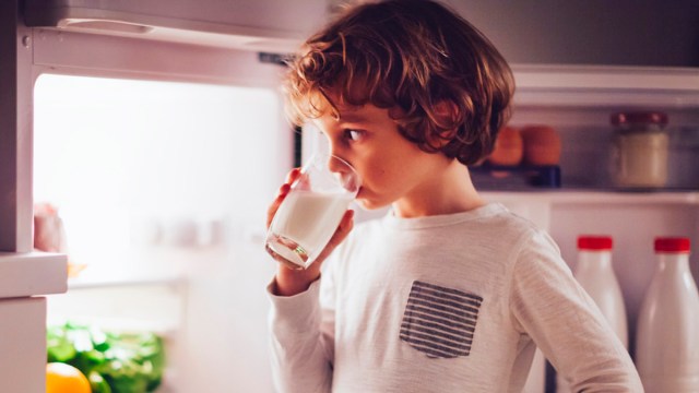 a kid having a bedtime glass of milk by the fridge for a story on the bedtime snacks to avoid